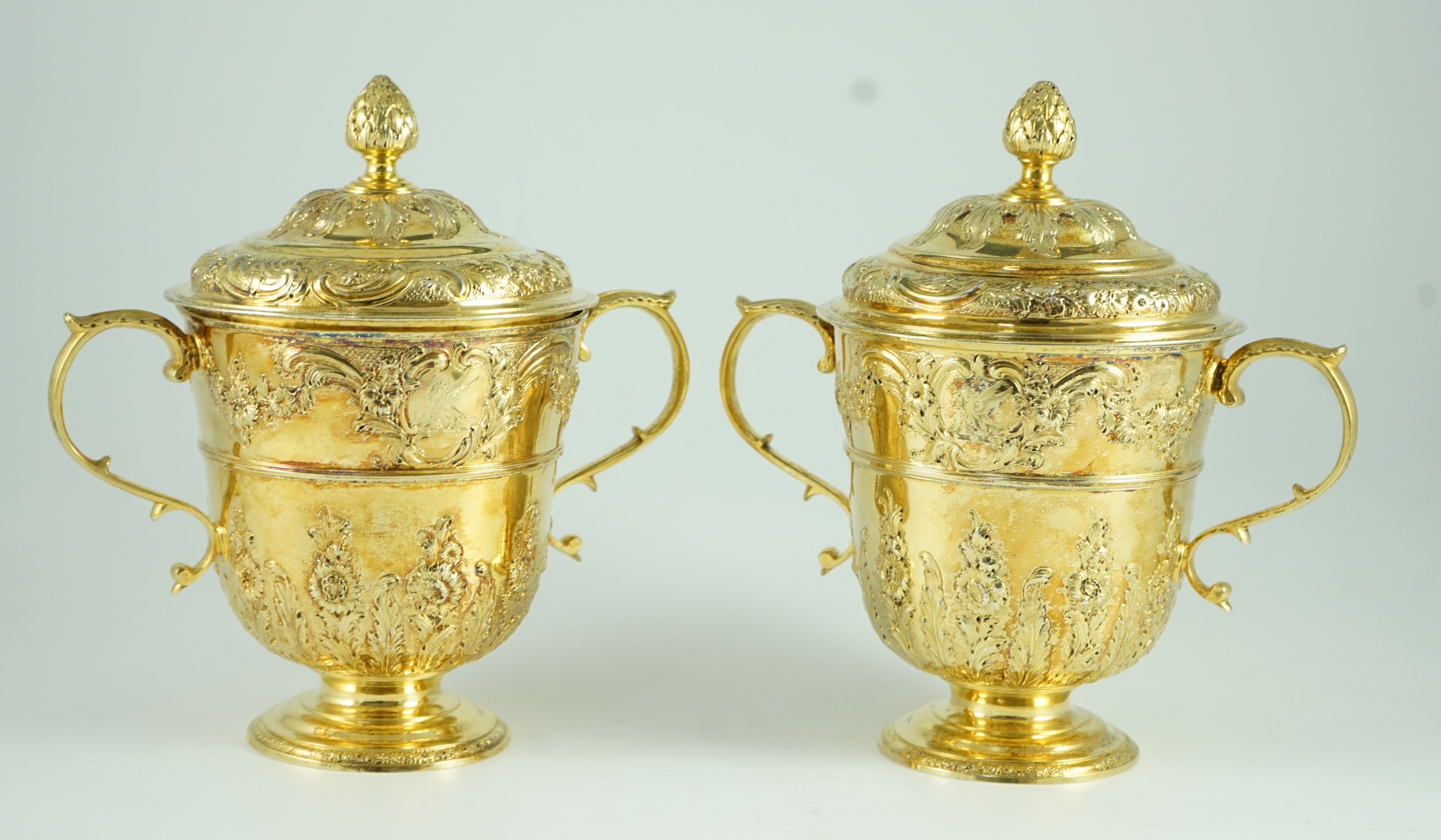 A good pair of George II embossed silver gilt two handled pedestal cups and covers, by Benjamin Gignac
